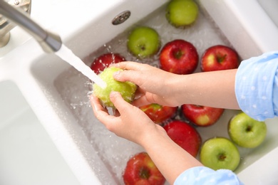 Photo of Woman washing fresh apples in kitchen sink, top view