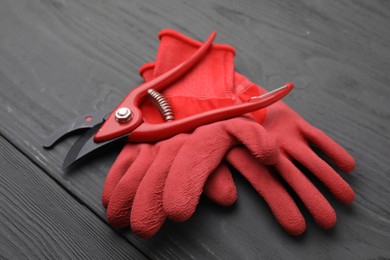 Pair of red gardening gloves and secateurs on grey wooden table, closeup