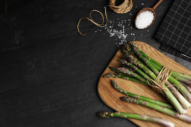 Photo of Fresh raw asparagus on black table, flat lay. Space for text