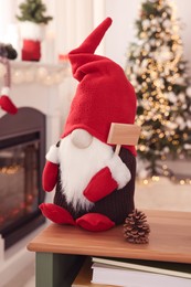 Photo of Cute Christmas gnome on wooden table in room with festive decorations