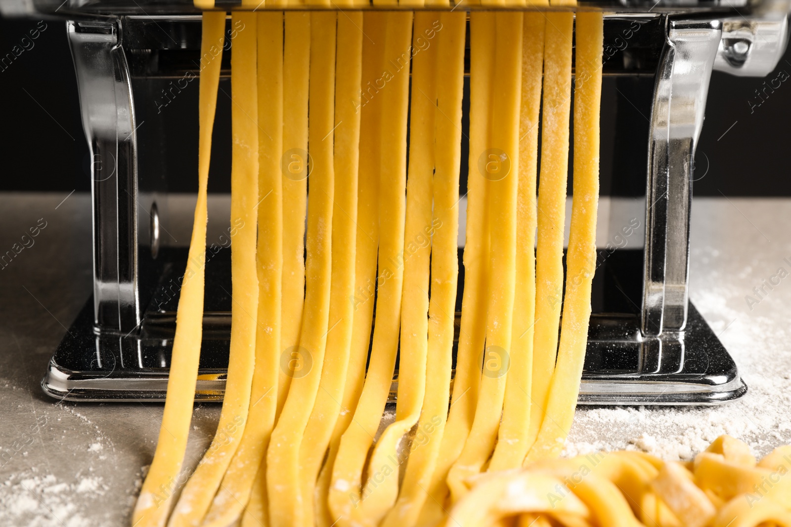 Photo of Pasta maker machine with dough on grey table, closeup