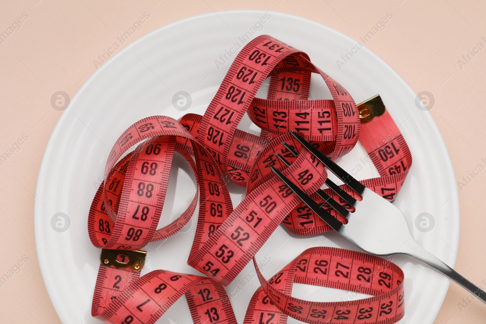 Photo of Plate, measuring tape and fork on beige background, top view. Diet concept