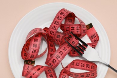 Photo of Plate, measuring tape and fork on beige background, top view. Diet concept