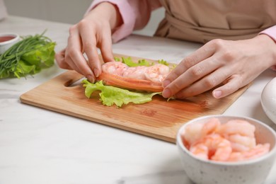 Photo of Woman making delicious spring roll at white marble table, closeup