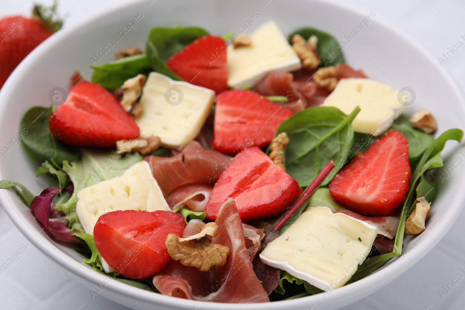 Photo of Tasty salad with brie cheese, prosciutto, strawberries and walnuts in bowl, closeup