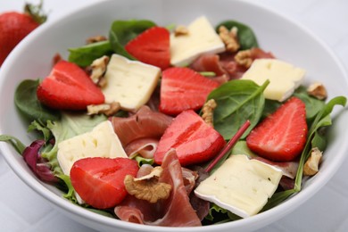 Photo of Tasty salad with brie cheese, prosciutto, strawberries and walnuts in bowl, closeup