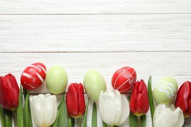 Photo of Flat lay composition of painted Easter eggs and spring flowers on wooden background, space for text