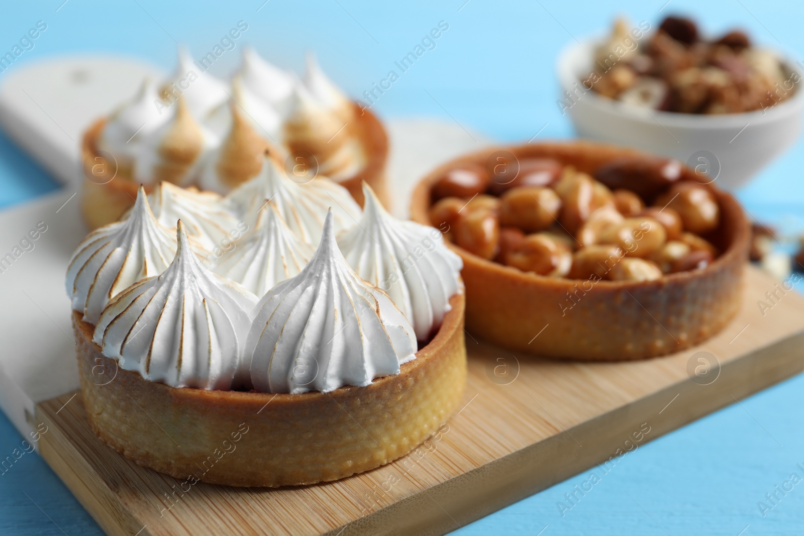 Photo of Different tartlets on light blue table, closeup. Delicious dessert