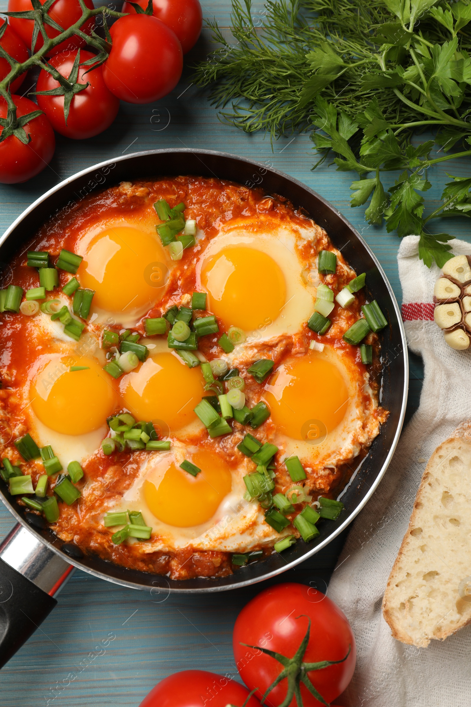 Photo of Delicious Shakshuka in frying pan served on light blue wooden table, flat lay