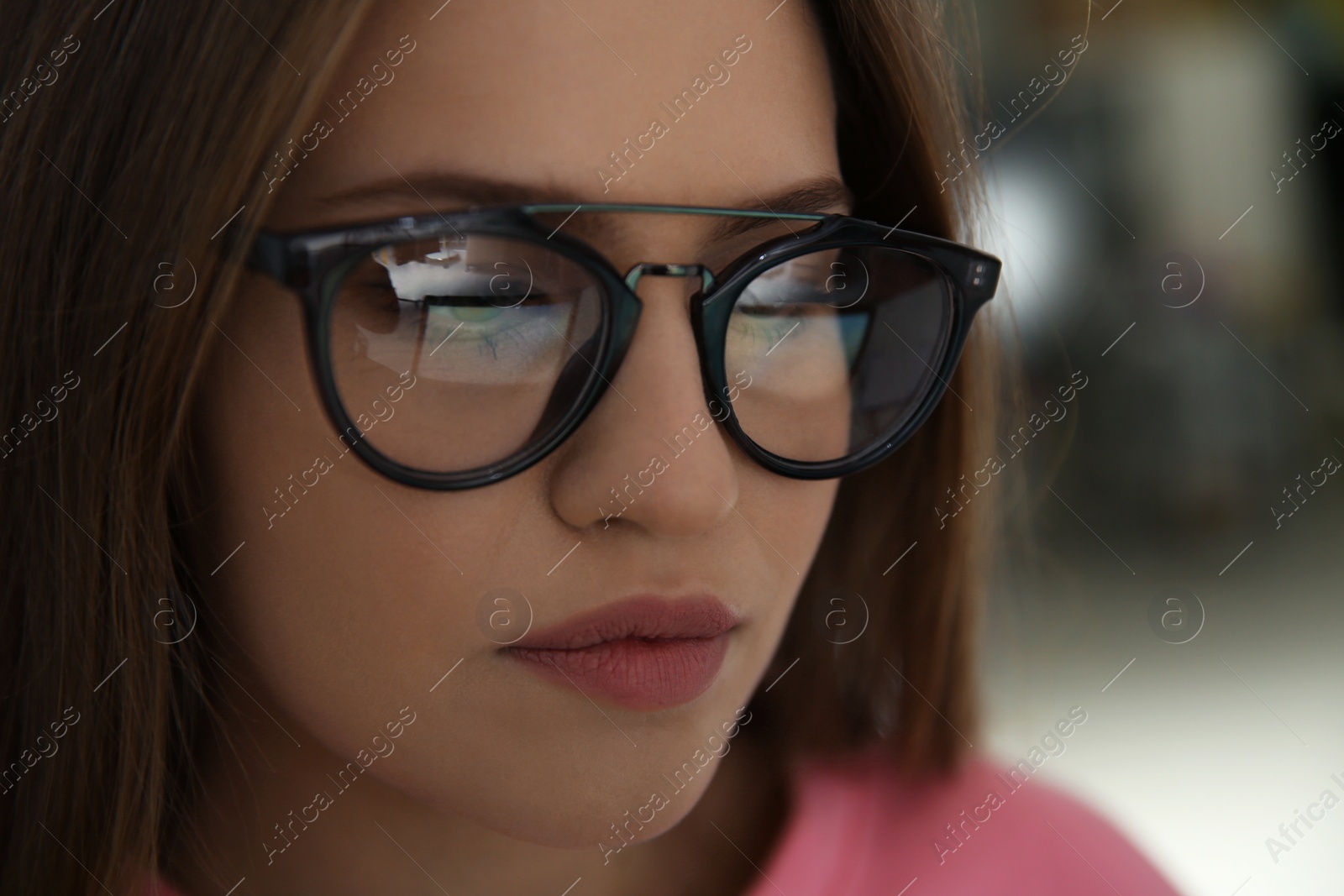 Photo of Young woman wearing glasses on blurred background, closeup. Ophthalmology service