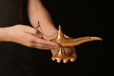 Photo of Woman rubbing magical Aladdin lamp on black background, closeup