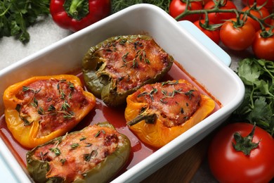 Photo of Tasty stuffed peppers in dish and ingredients on table, closeup