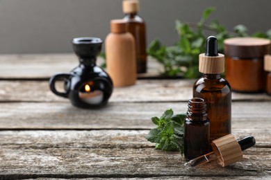 Photo of Bottles of mint essential oil and fresh leaves on wooden table, space for text