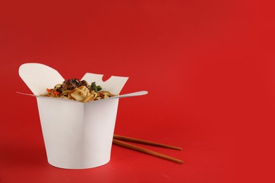 Photo of Box of wok noodles with vegetables, meat and chopsticks on red background. Space for text