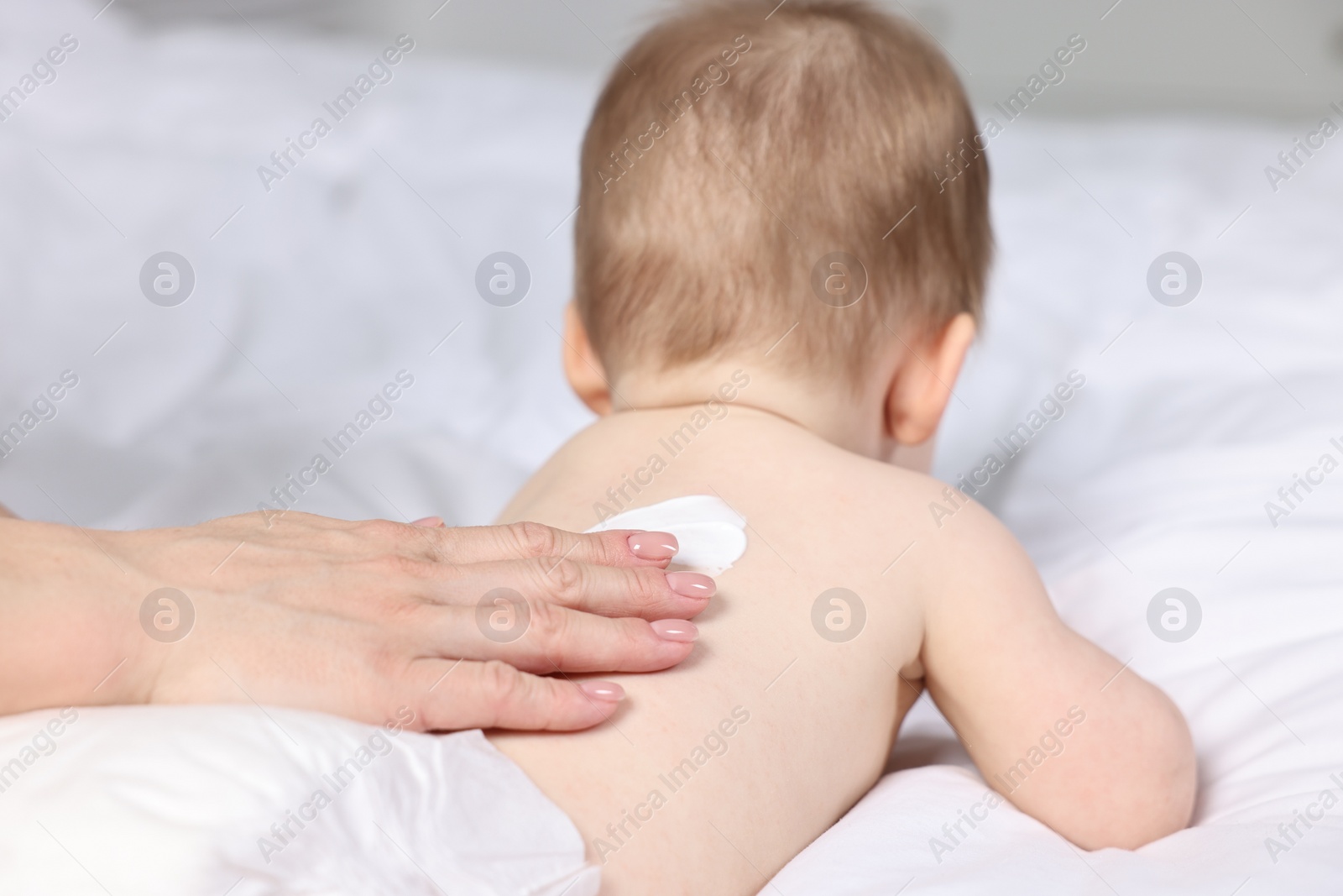 Photo of Woman applying body cream onto baby`s back on bed, closeup