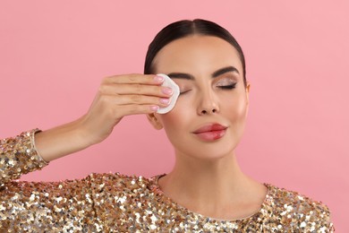 Beautiful woman removing makeup with cotton pad on pink background