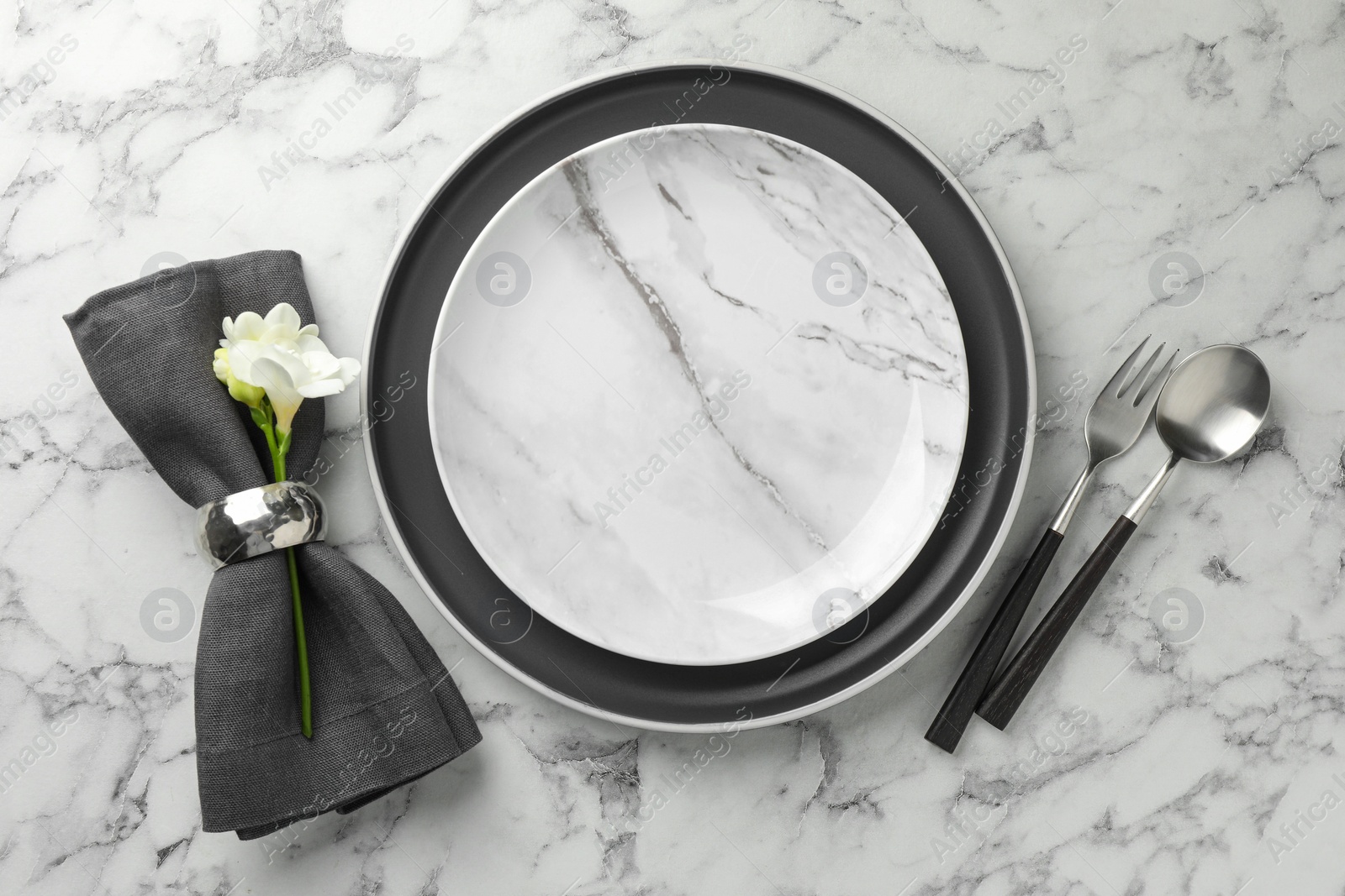 Photo of Stylish setting with cutlery, napkin, flowers and plates on white marble table, top view