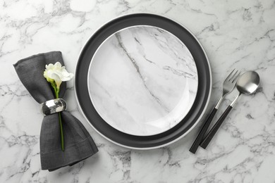 Stylish setting with cutlery, napkin, flowers and plates on white marble table, top view