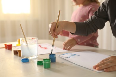 Little children drawing with brushes at wooden table indoors, selective focus