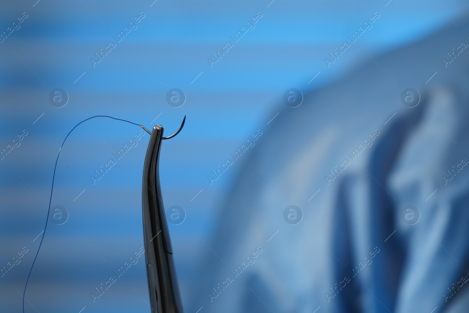 Photo of Forceps with suture thread on blurred background, closeup. Medical equipment