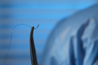 Photo of Forceps with suture thread on blurred background, closeup. Medical equipment