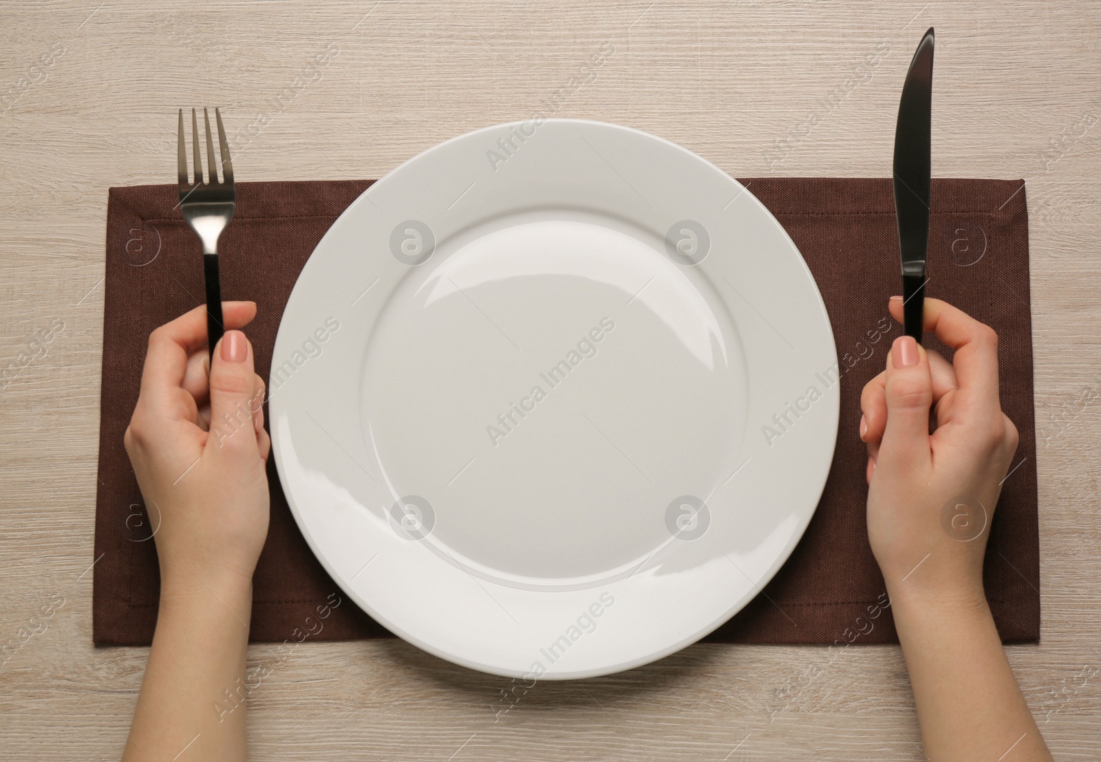 Photo of Woman with empty plate and cutlery at wooden table, top view