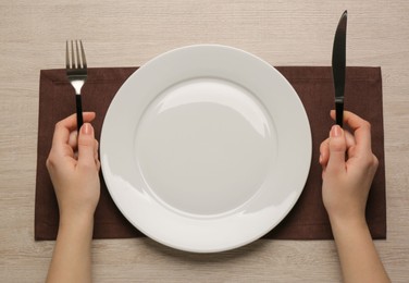 Woman with empty plate and cutlery at wooden table, top view