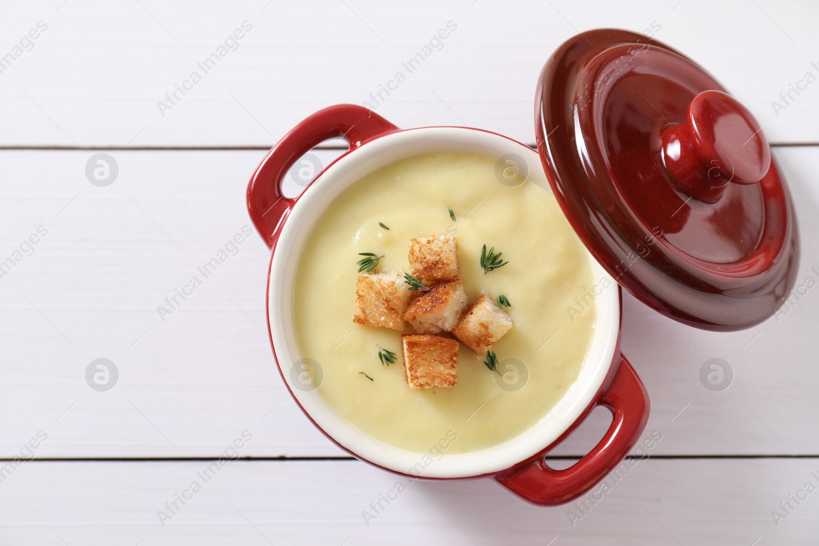 Photo of Tasty potato soup with croutons and rosemary in ceramic pot on white wooden table, top view. Space for text