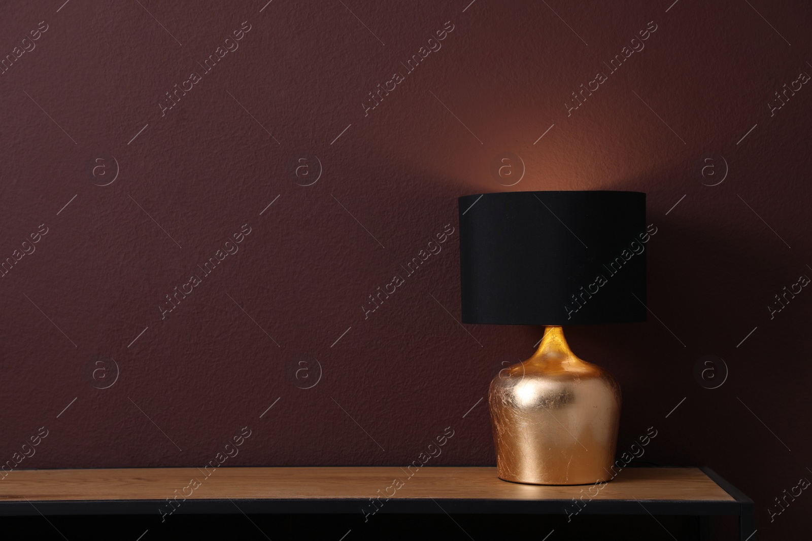 Photo of Wooden table with lamp near brown wall in room, space for text