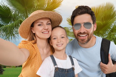 Image of Happy family with child taking selfie near palm trees outdoors