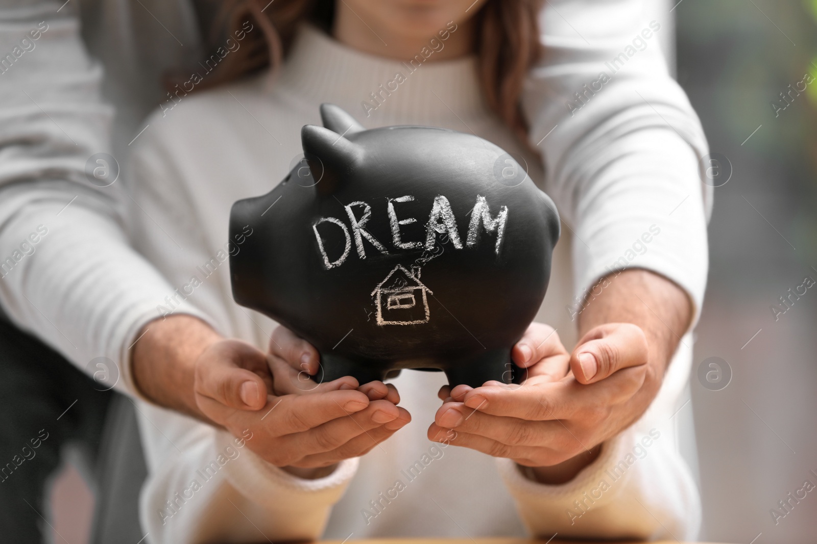 Photo of Couple holding piggy bank with word DREAM, closeup