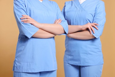 Nurses in medical uniforms on light brown background, closeup