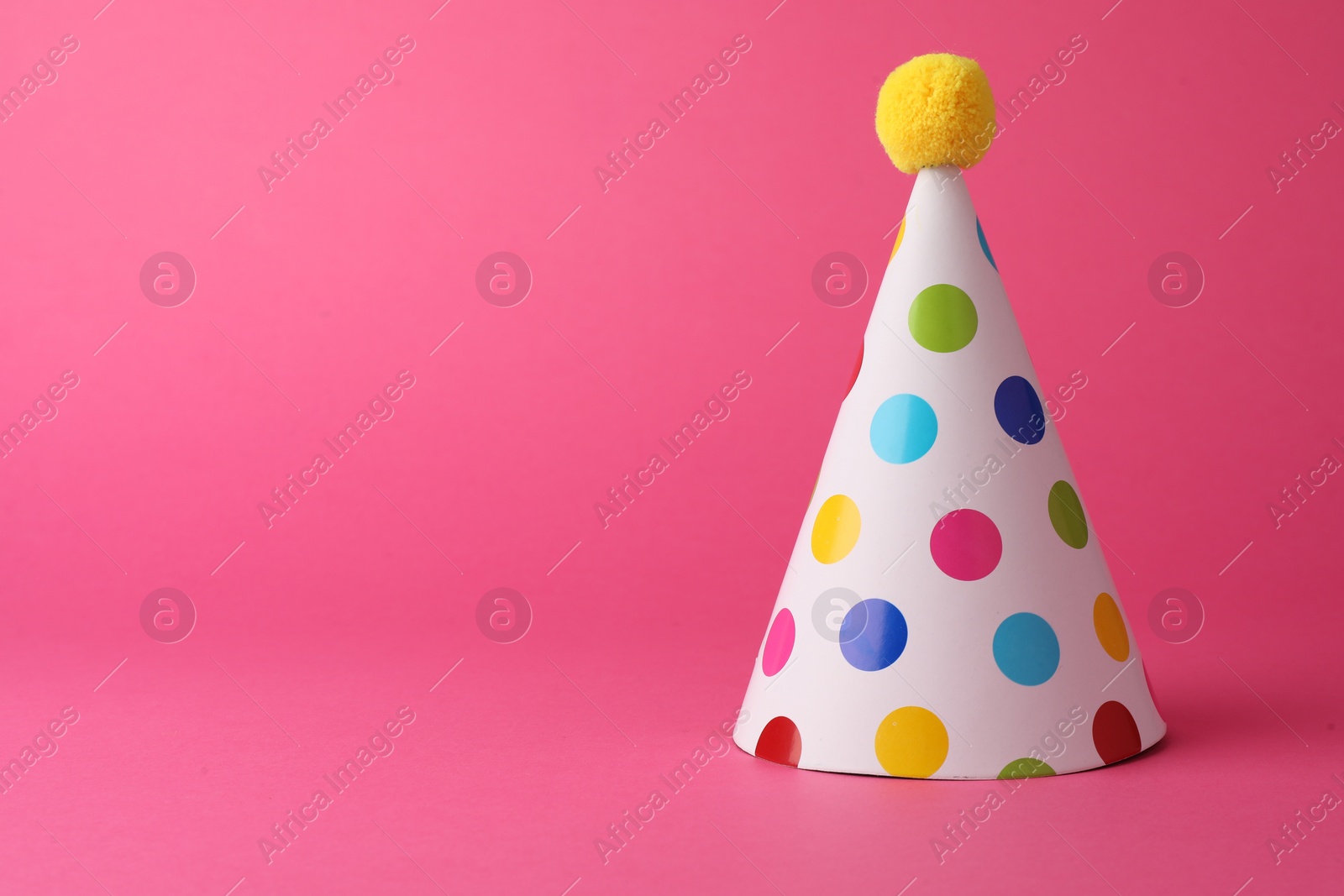 Photo of One beautiful party hat with pompom on pink background, space for text