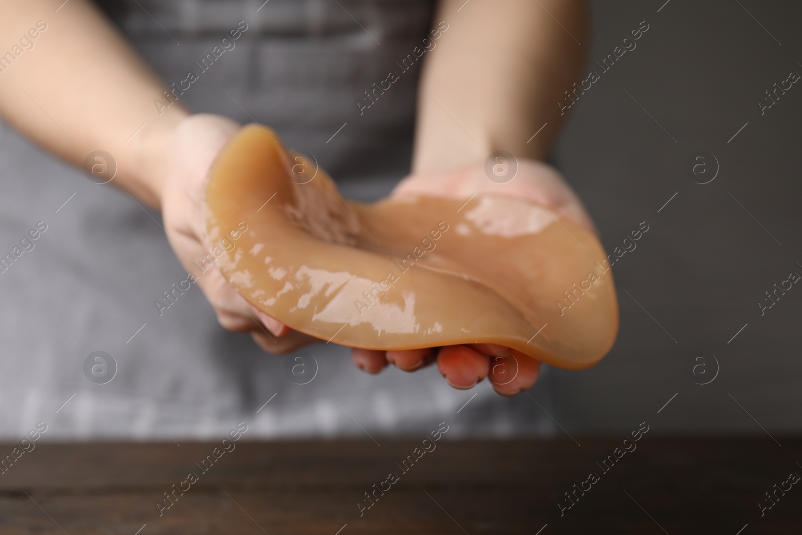 Photo of Making kombucha. Woman holding Scoby fungus at wooden table, closeup