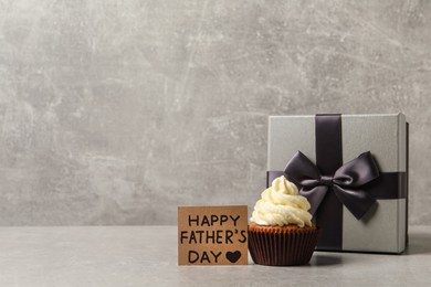 Photo of Card with phrase HAPPY FATHER'S DAY, tasty cupcake and gift box on grey background. Space for text