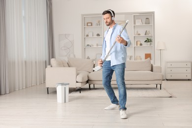 Photo of Happy man in headphones having fun with mop while cleaning at home