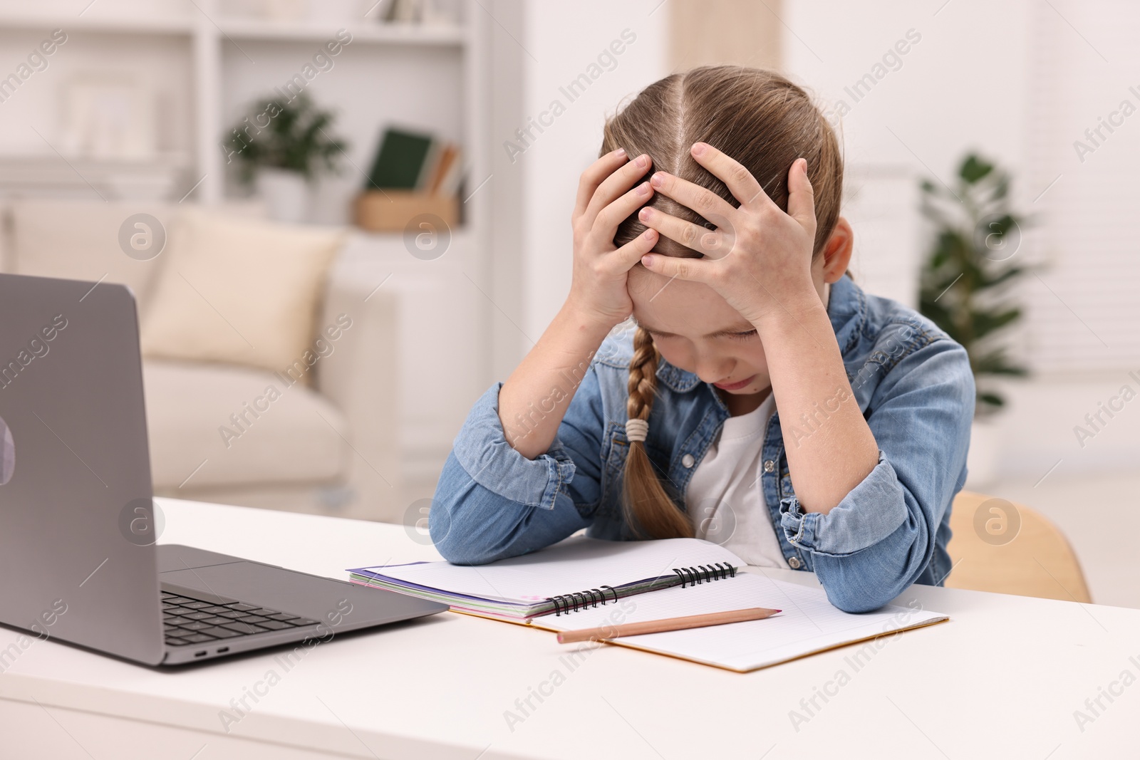 Photo of Little girl suffering from headache while doing homework at home