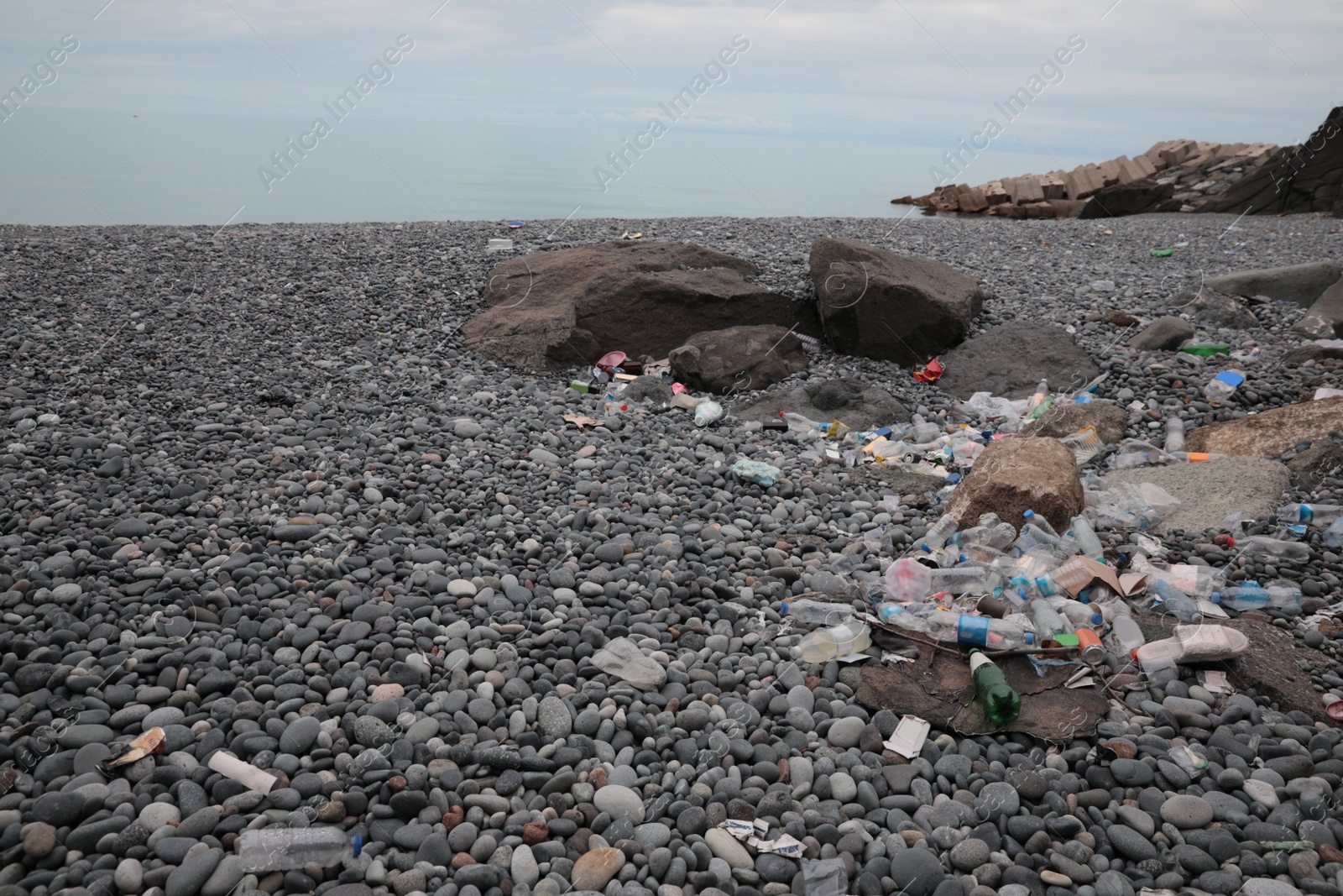 Photo of Garbage scattered on pebbles near sea. Recycling problem