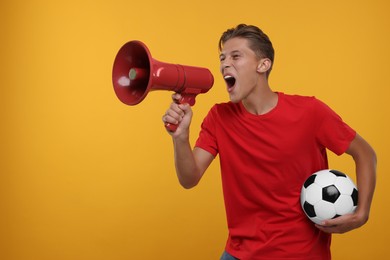 Photo of Sports fan with soccer ball shouting in megaphone on orange background. Space for text