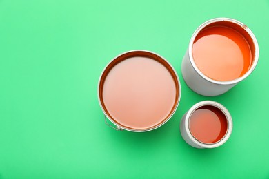Photo of Cans of orange paint on green background, top view. Space for text