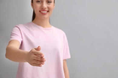 Photo of Happy young woman offering handshake on light grey background, closeup. Space for text