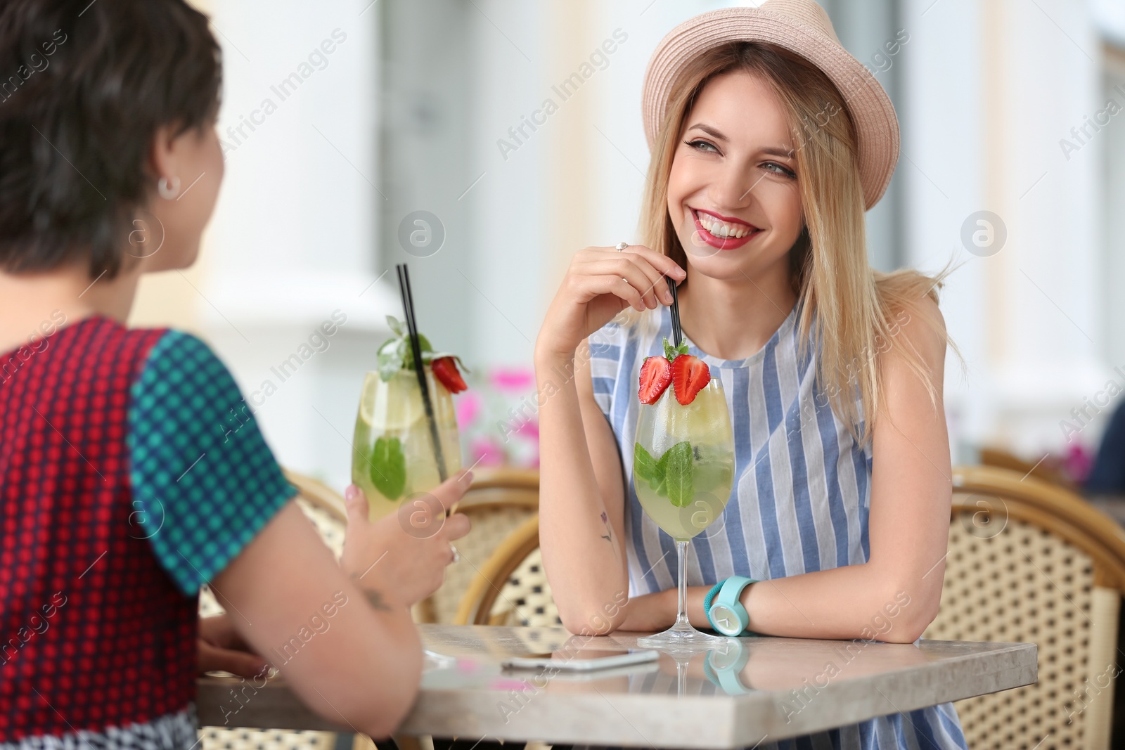 Photo of Young women with glasses of tasty lemonade in open-air cafe