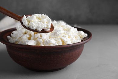 Clay spoon with cottage cheese above bowl on grey table, space for text