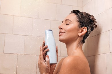 Photo of Young woman with bottle of shampoo in shower at home. Washing hair