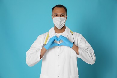 Photo of Doctor or medical assistant (male nurse) with protective mask and stethoscope making heart on turquoise background