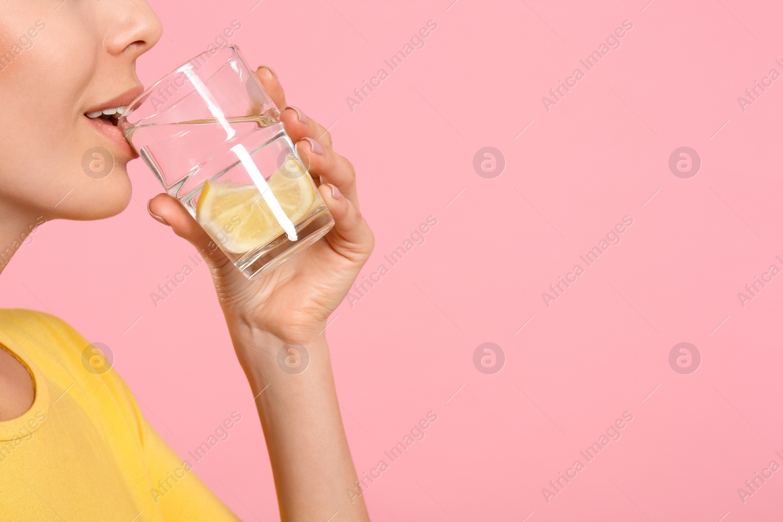 Photo of Young woman drinking tasty lemon water on pink background, closeup. Space for text