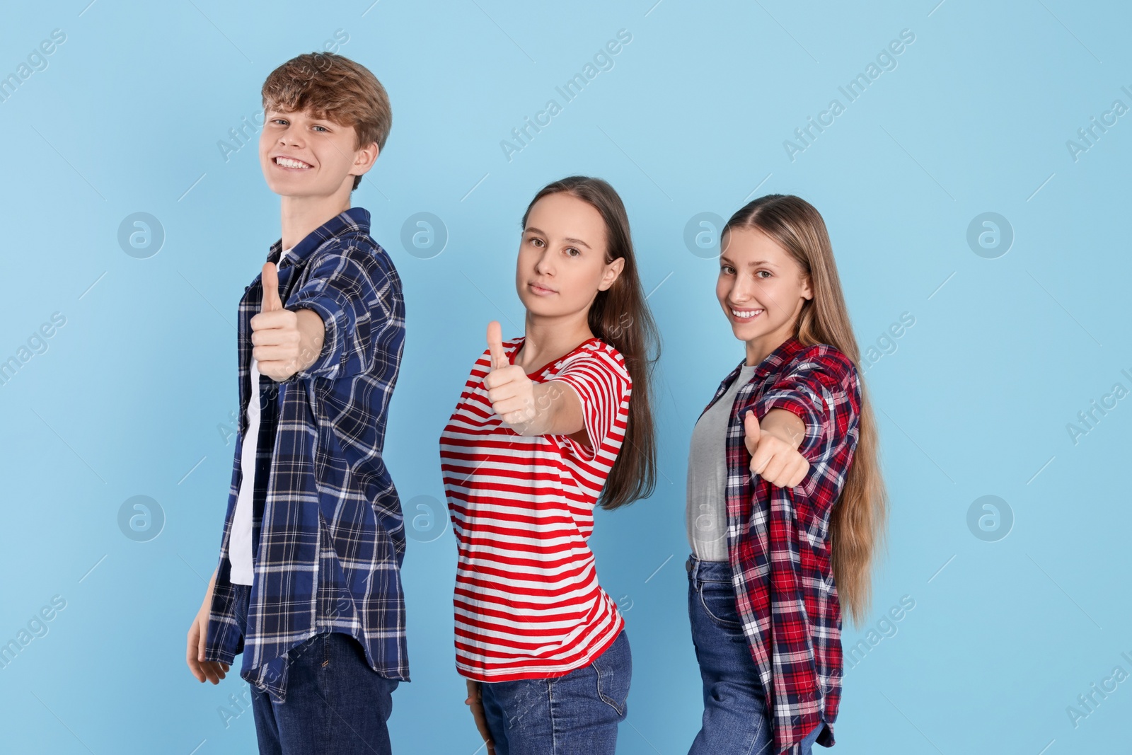 Photo of Group of happy teenagers showing thumbs up on light blue background