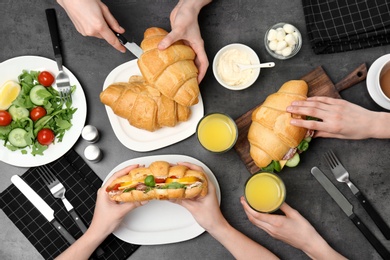 People eating tasty croissant sandwiches at table