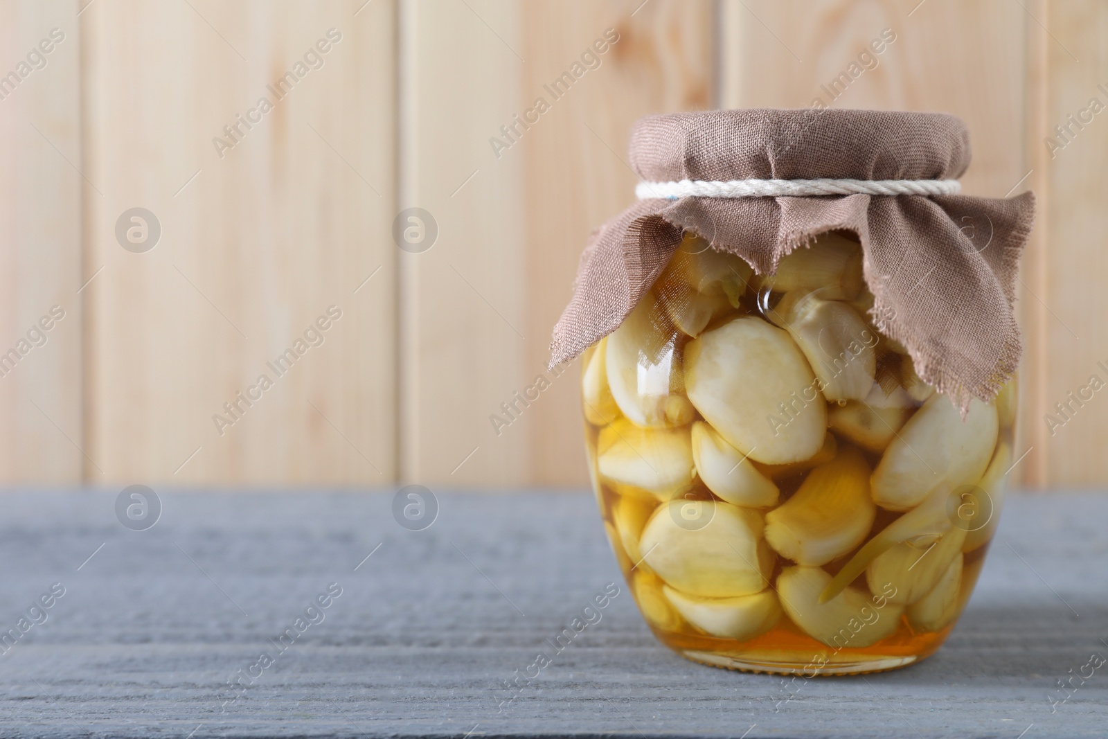 Photo of Garlic with honey in glass jar on grey wooden table. Space for text