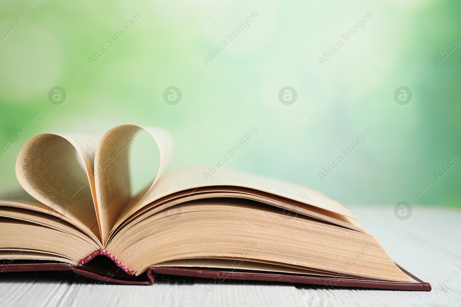 Photo of Open book on white wooden table against blurred green background, closeup